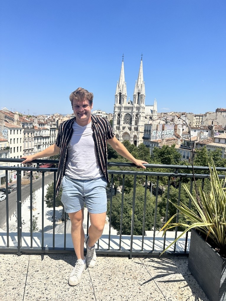 Calvin Pawlowski stands on a balcony overlooking a city and cathedral